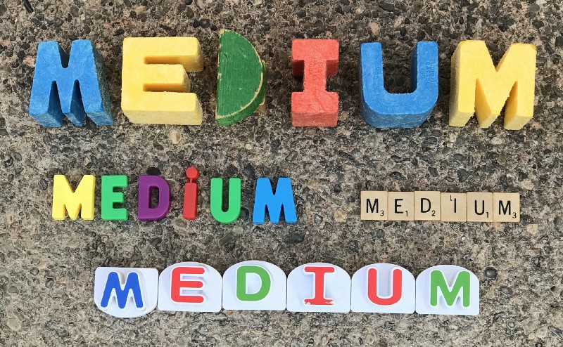 The image contains the word “Medium” spelled out with wooden blocks, magnetic letters, Scrabble tiles, and letters from a children’s game.