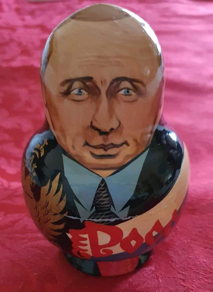 There is a photo of a matryoshka (Russian nesting) doll with the face and body of Vladimir Putin with a red background.  