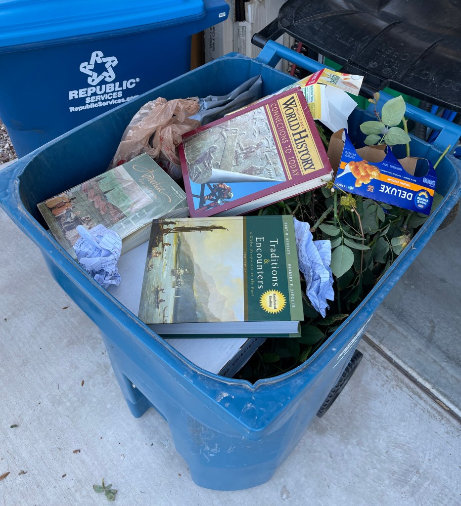 Garbage can filled with trash with history books on top