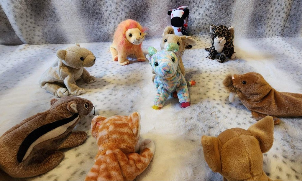Photo of eight Beanie Babies placed around a bunny Beanie Baby humping a colorful ram Beanie Baby on a gray and white background. The ram looks disturbed.